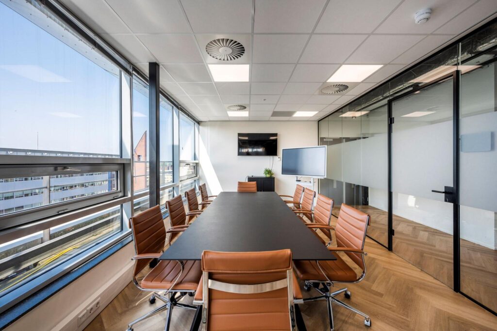 Modern conference room at Bos en Lommerplein with a large table, leather chairs, and glass walls.